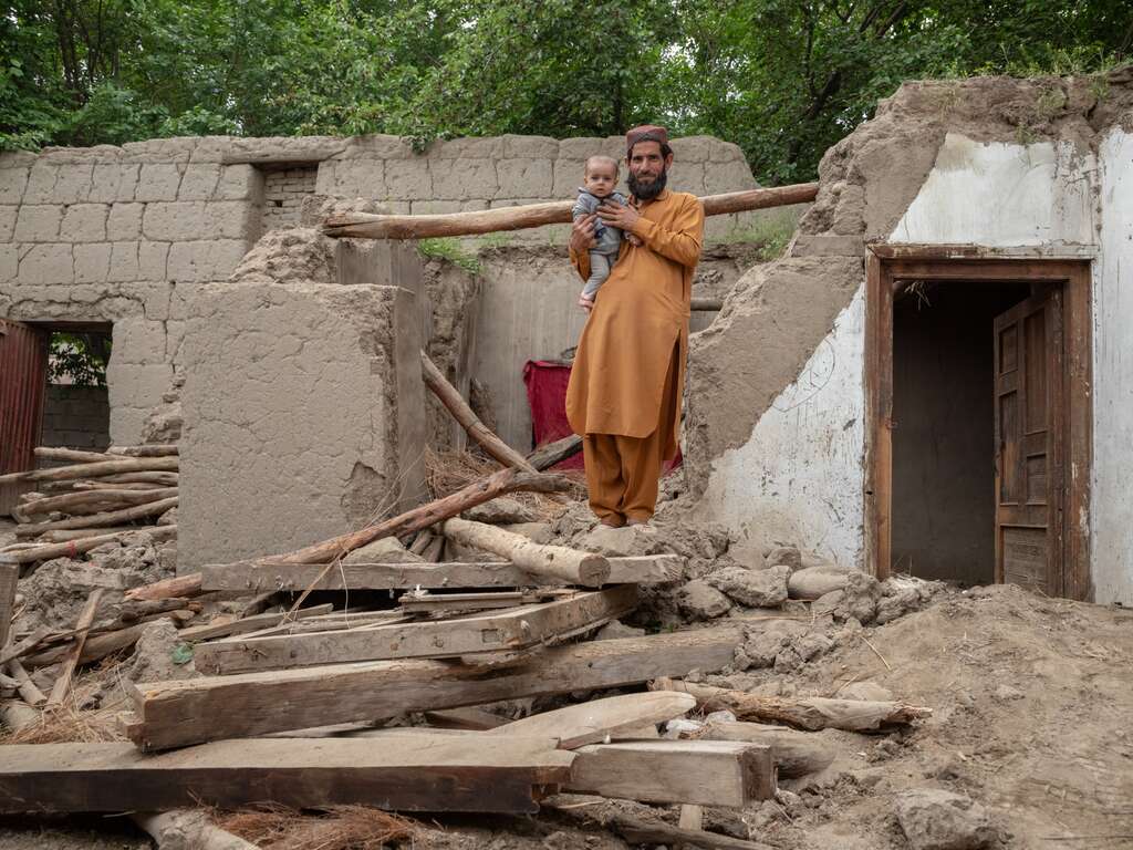 A man holds his son and walks through the remnants of their home in Afghanistan.