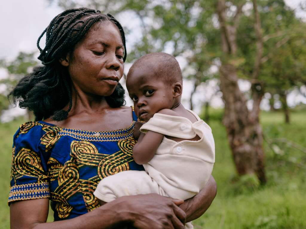 A mother holds her young daughter in her arms as they walk outside.