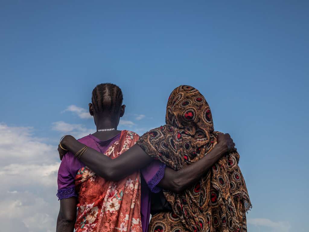 Two women stand together with one arm over each other's shoulder in South Sudan.