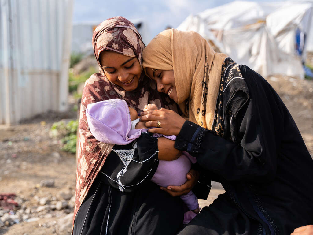 Ruwaidah och hennes vän Maryam tittar på Ruwaidahs nyfödda barn Mortada i ett flyktingläger i Jemen.