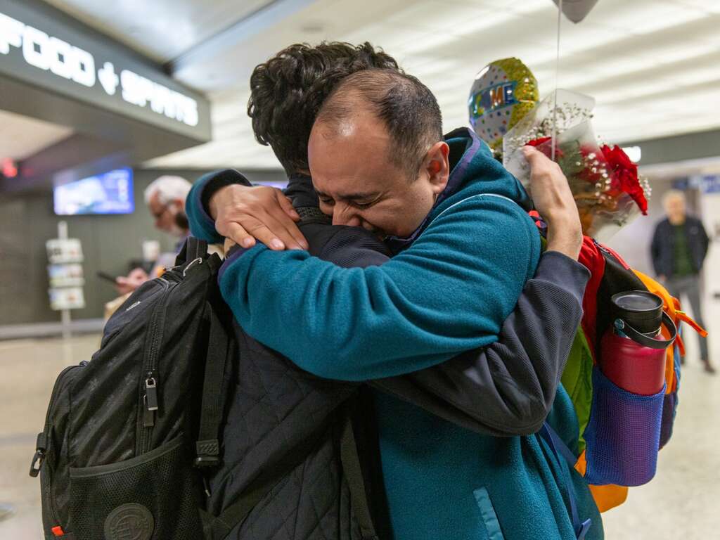 Two people embrace at an aiport after reunifying.