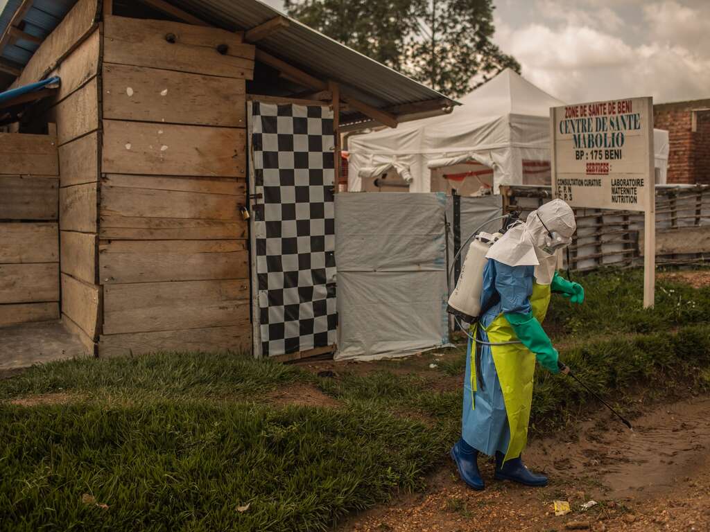 A health worker in full protective gear sprays disinfectant outside a health center in Beni, DRC.