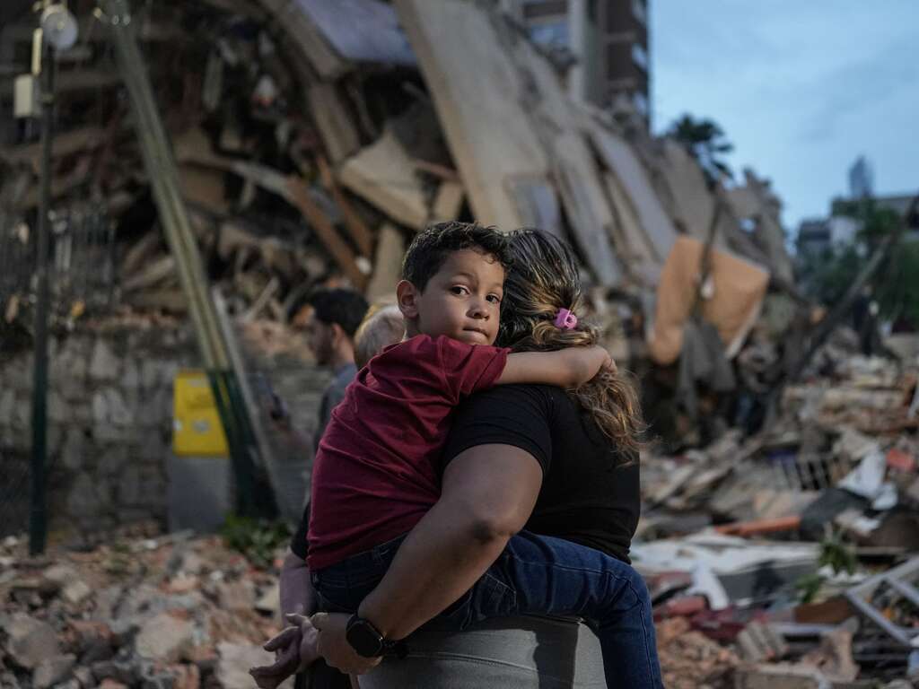 A person carries a child in front of a pile of rubble and destroyed buildings after an earthquake in Venezuela.