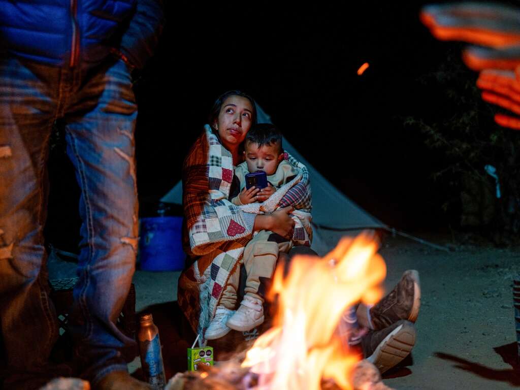 A child and his mother stay close near a campfire.