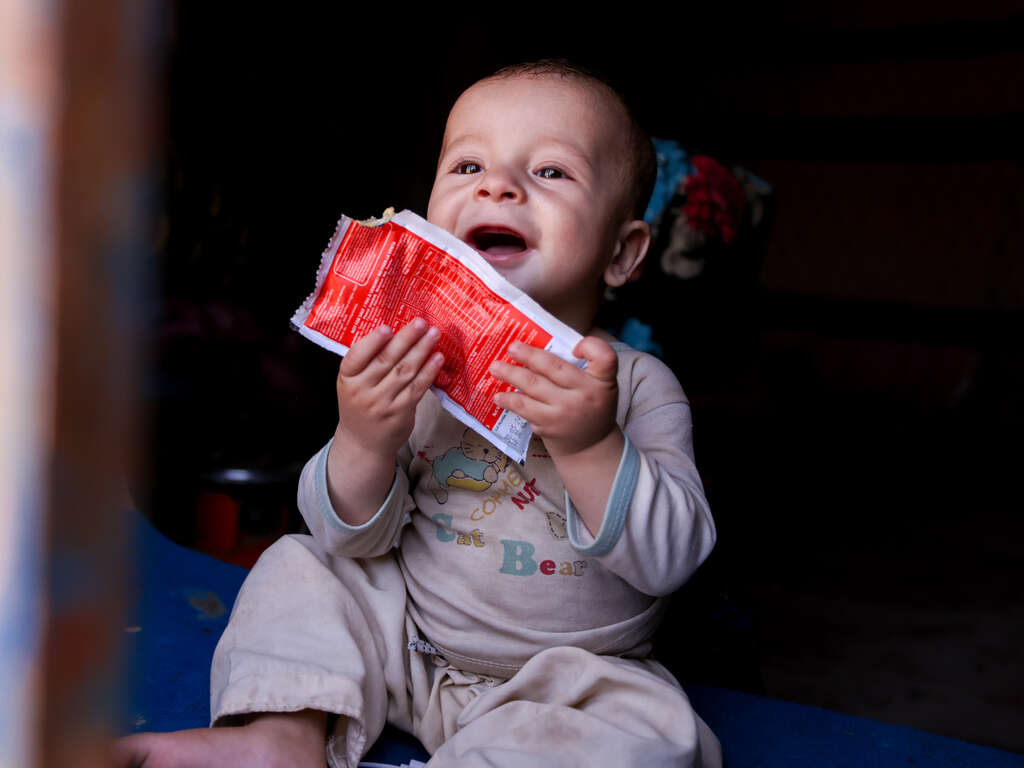 Child smiling with open packet of nutrition supplement