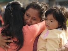 Eine Frau hält ein Kind im Arm, weint und umarmt eine andere Frau.