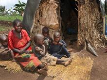 Eine Mutter sitzt mit ihren Kindern vor einer einfachen Hütte aus Holz