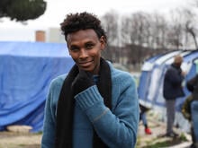 Ein junger Mann schaut in einem Lager in die Kamera und lächelt