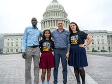 Members of the IRC's Refugee Voices program, two men and two women, stand in front of the U.S. Capitol. The women are wearing shirts that say Refugees Welcome. 
