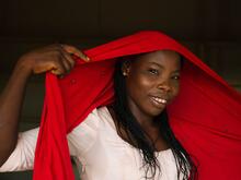 A girl holding a red scarf over her head.