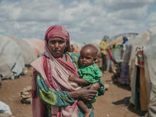 Mother stands holding her 12 month baby, in Daryel Shabellow IDP camp, Somalia.