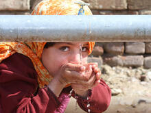 A child cupping their hands to drink clean water from a spigot.