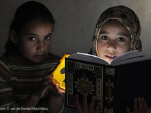 Two girls reading a book together using a solar lamp.