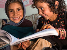 Two girls read together by the light of their solar lamp.