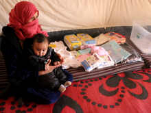 A Syrian mother and baby next to a baby kit of clothing, diapers and other essentials