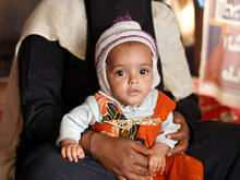 A young Yemeni child is held by their parent.