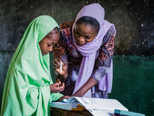 A teacher and a student read together from a text book.