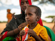 A boy eats fortified peanut paste in Olol Village, Somalia, while sitting on his mother's lap