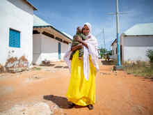 Fartun stands in the street, holding her baby son.