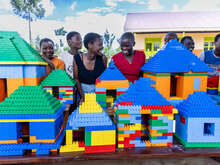 Students stand beside an entire village they made using LEGO bricks, containing houses, schools, churches and mosques.