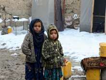 Two children stand in snow outside their home