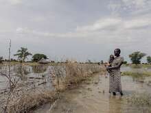 A woman holding a baby and standing in a flooded field.