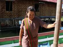 A woman on a boat wearing a brown shirt and carrying a pink and green crossbody bag looks down and smiles