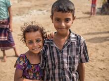 예멘에서 어린 여자아이와 남자아이가 화창한 날 집 밖으로 나와 미소 짓고 있습니다.