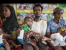 Surrounded by other waiting families, a man holds a young child he has brought to an IRC health center in Myanmar for treatment.