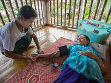 An IRC health worker takes the blood pressure of a female patient lying on a mat on the floor in Thailand.