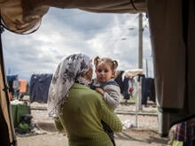 A mother holds her toddler daughter and looks out from their tent on a cloudy day in a refugee camp in Idomeni, Greece.