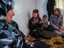 An IRC staff member talks with a Syrian refugee family seated on cushions in their shelter in Zaatari refugee camp in Jordan.