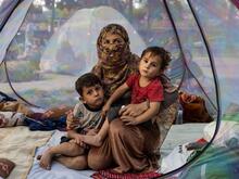 A recently widowed Afghan woman, 28, sits on the floor of a net tent holding holding her two children in a makeshift camp for displaced families in Afghanistan.