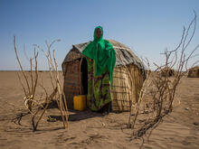 Woman stands in front of temporary shelter in drought-afflicted region.