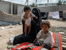 A mother and her two young children seated outdoors in Yemen