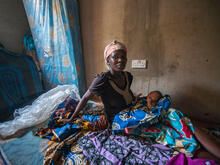 A Nigerian woman sits on a mattress with her infant child.