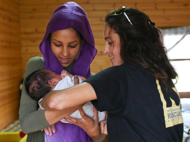  En kvinna håller ett barn och en annan kvinna hjälper henne.
