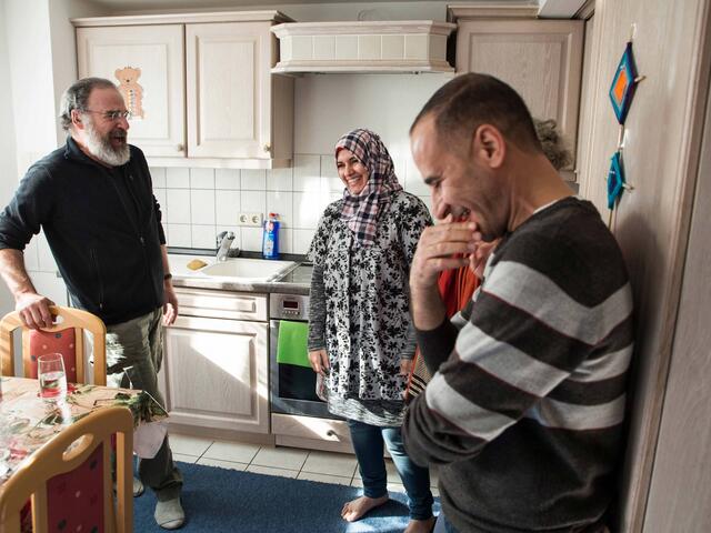 Mandy, Koder und seine Frau stehen in der Küche und lachen herzlich.