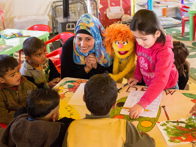 En förskole klass sitter vid ett bord med en av mupparna från det amerikanska barnprogrammet Sesame street