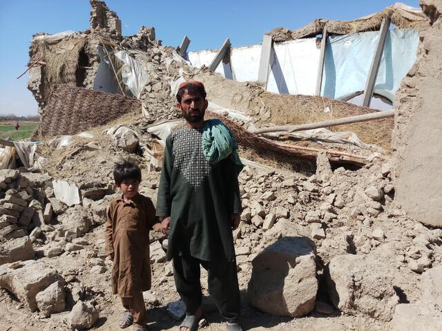 A man and a boy standing in front of a destroyed house
