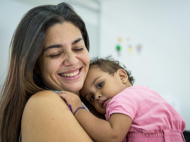 A woman is smiling and has her Baby lying on her chest