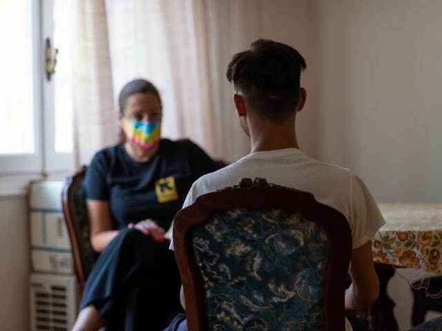 An adolescent boy and a woman wearing a mask sitting facing each other