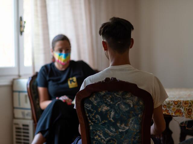 An adolescent boy and a woman wearing a mask sitting facing each other