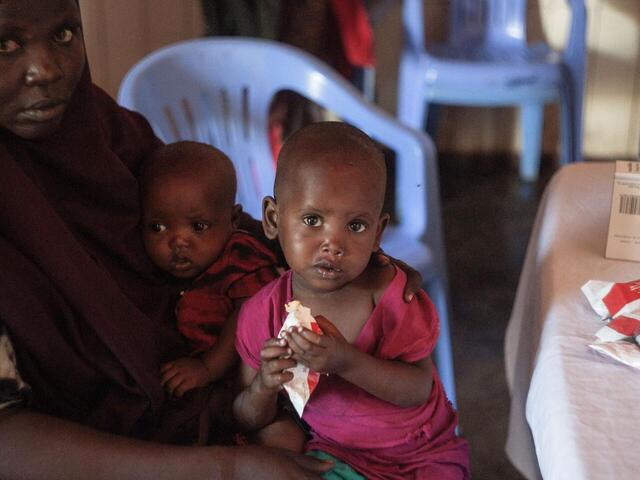 A mother with two children is sitting together, as one of the children eats plumpynut.