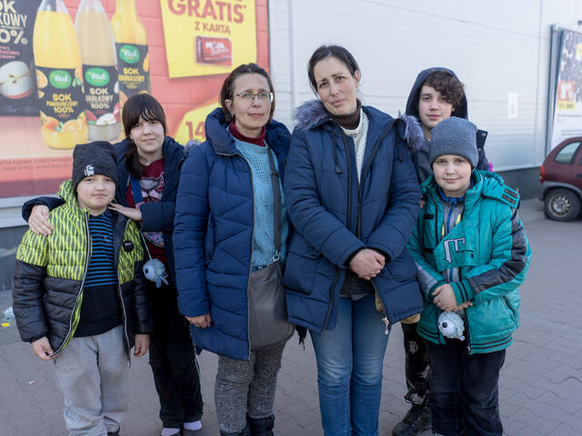 Two sisters stand together in a parklng lot. Each sister has her own two kids with her.