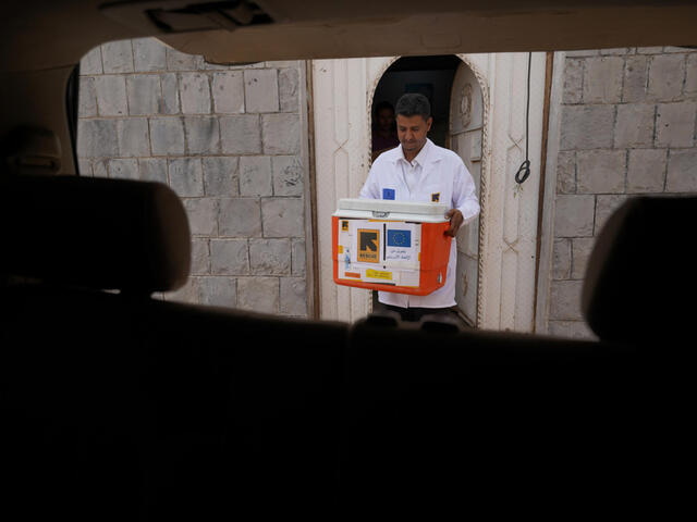 Pharmacist in white coat carrying orange box to the car