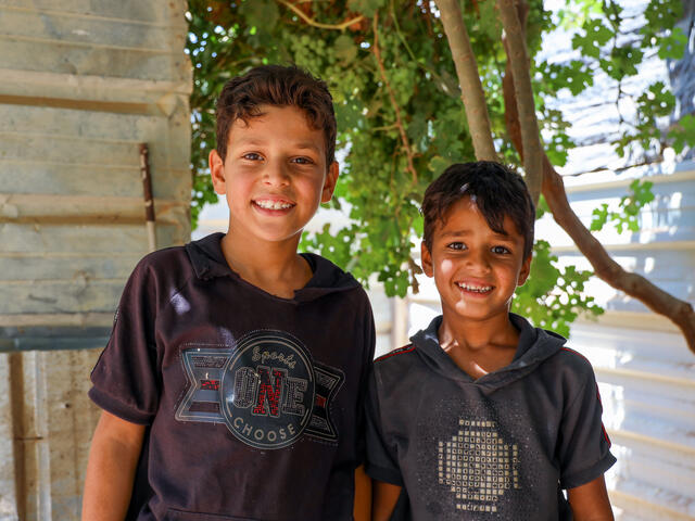 10-year-old and 8-year old Syrian brothers stand in the shade behind their family's container home in a refugee camp in Jordan