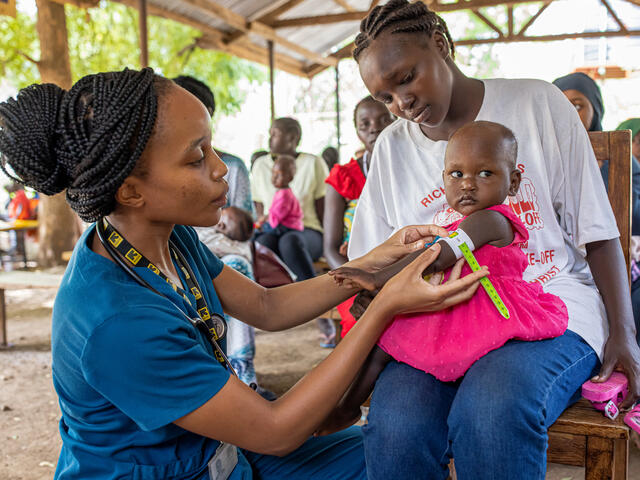 An IRC doctor treats a one year old girl who sits on her mother's lap