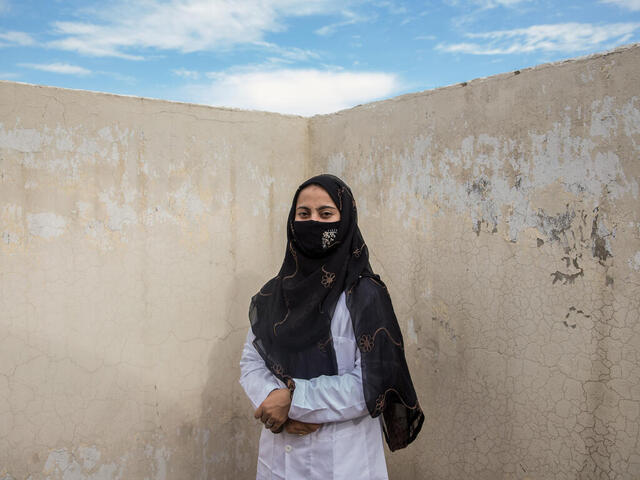 A female doctor in a white coat stands against a wall