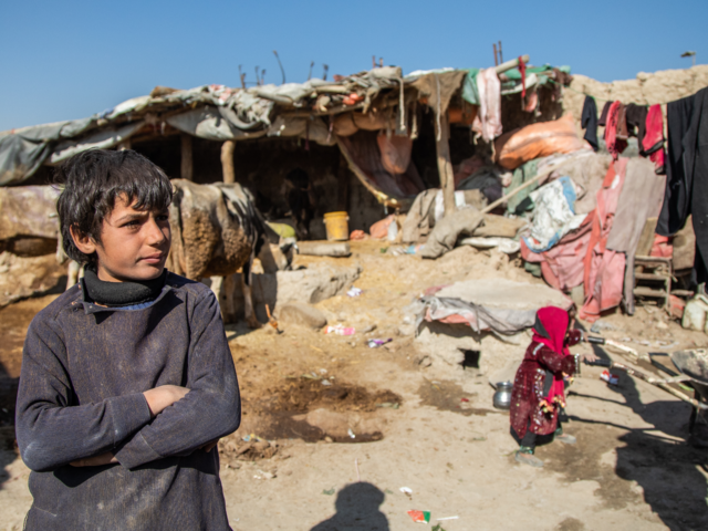 A boy, living in Ghaibi Bala camp in Kabul, Afghanistan, looks on as his mother is interviewed by International Rescue Committee (IRC) staff to see if she meets the criteria to receive a cash distribution from the IRC. The impact of Afghanistan's economic problems is evidenced by the conditions of his surroundings.
